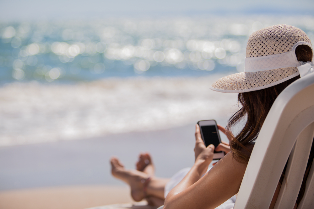 Jeune femme sur un transat à la plage consultant son téléphone mobile.